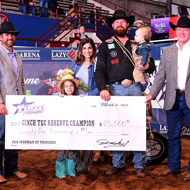 A group of people holding a large white check smiling and posing wearing western attire. 